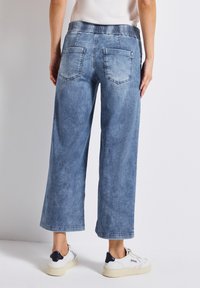 Pantalons en denim bleu clair à jambes larges avec une taille élastique, deux poches arrière et une texture délavée. L'ourlet retroussé crée un look décontracté.