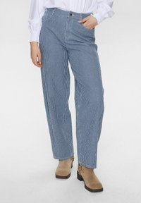 Pantalons larges à rayures bleu et blanc, avec une taille haute, un fermeture à bouton et une coupe décontractée. Assortis à des bottines beiges.