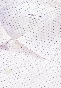 Biała koszula z niewielkim fioletowym wzorem, z standardowym kołnierzykiem, listwą z guzikami i metką z napisem "seidensticker". Gładka faktura.