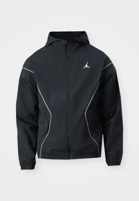 Veste coupe-vent noire avec capuche, surpiqûres blanches et logo brodé sur la poitrine. Poignets et ourlet élastiques pour un ajustement confortable.