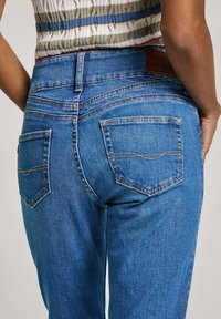 Blå denimjeans med en midjehöjd av medelhöjd, har två bakfickor, subtila sömnadsdetaljer och en jämn textur.
