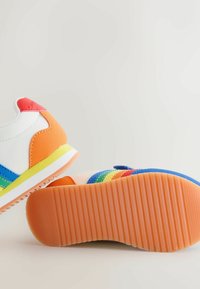 Värikkäät tennarit, joissa on valkoinen kangaspäällinen, oransseja ja sinisiä yksityiskohtia, uritettu kumipohja ja moniväriset raidat.