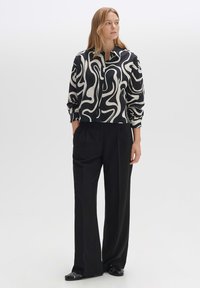 Blusa a righe in bianco e nero con colletto, maniche lunghe e chiusura a bottoni, abbinata a pantaloni neri a vita alta e sandali.