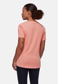 Kortærmet ferskenfarvet t-shirt med rund halsudskæring, slidser i siderne og et "Mammut" logo på den bageste krave. Lavet af blødt, åndbart bomuld.