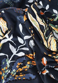 Mörk tyg med ett färgglatt botaniskt mönster som har vita blad och abstrakta former i orange, grönt och blått, lätt skrynkligt.