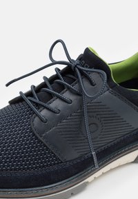 Navy blue sneaker with mesh and leather upper, green lining, textured accents, and matching laces. Features a cushioned sole for comfort.