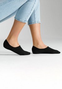 Schwarze Knöchelsocken mit einer weichen, glatten Textur und minimalistischem Design, kombiniert mit hellblauen, hochgekrempelten Jeans, die einen tiefen Ausschnitt zeigen.