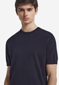 Mörkblå kortärmad t-shirt med rundad hals i ett mjukt tyg med en figurnära silhuett. Ribbade kragar och ärmslut, minimalistisk design.