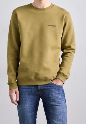 Mand iført olivengrøn crewneck-sweatshirt med "DONDUP" logo på brystet og blå jeans, hånd i lommen mod en neutral baggrund.