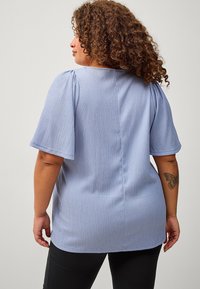 Light blue textured top with short puff sleeves, round neckline, and a straight cut. Features subtle vertical stripes and a back seam detail.