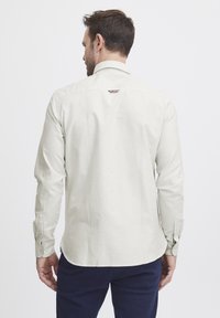Lysfarget, stripete skjorte med knapper og lange ermer. Har en klassisk krage, mansjetter og en liten aksentetikett bak.