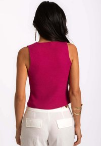 Top sin mangas fucsia con textura acanalada y un diseño ajustado, combinado con pantalones blancos que tienen bolsillos traseros.