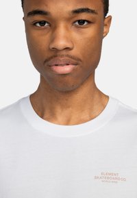 Hvid bomulds t-shirt med rund hals og et lille pink logo på venstre bryst, der står "ELEMENT SKATEBOARD CO. WORLD WIDE."
