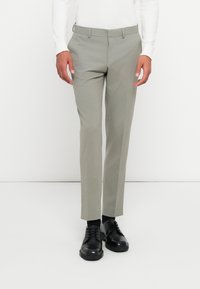 Világosszürke, slim fit szabású nadrág, sima tapintással és övhurkokkal. Fekete fűzős cipővel viselve.