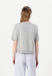 Maglione corto grigio a maniche corte con colletto e orlo a costine, caratterizzato da un design cropped. Materiale a maglia testurizzata, indossato con pantaloni a righe.