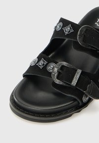 Black suede sandals with dual adjustable straps featuring silver hardware embellishments. Contoured footbed with a textured, durable sole.