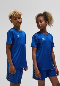 Blå atletisk tröja och shorts i mjukt, lättviktigt tyg. Har svarta detaljer på axlar och sidor samt en logotyp på bröstet.