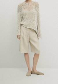 Lichtbeige gebreide trui met een open structuur, gecombineerd met beige shorts tot de knie en lichte, platte schoenen. Eenvoudig en casual ontwerp.