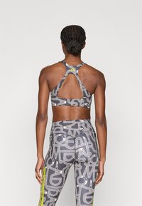 Σετ αθλητικού σουτιέν και κολάν σε γκρι με λευκά αφηρημένα μοτίβα. Το σουτιέν έχει σχεδιασμό racerback· το κολάν διαθέτει φωτεινή κίτρινη λεπτομέρεια.