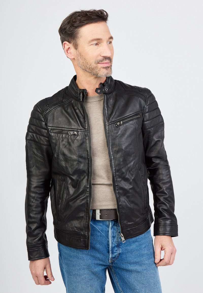 Schwarze Lederjacke mit einem Reißverschluss vorne, Druckknopfkragen, gerippten Schulterdetails und zwei Brusttaschen, getragen über einem grauen Hemd und blauen Jeans.