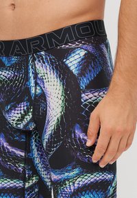 Collants avec un motif vibrant d'écailles de serpent dans des teintes de bleu et de vert, dotés d'une taille élastique noire affichant "ARMOUR" en lettres majuscules.