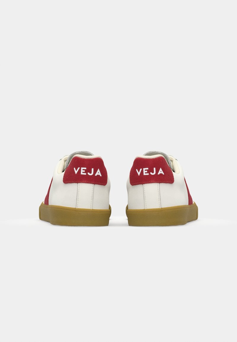 Sneaker con una toma bianca in pelle, dettagli in camoscio rosso sul tallone e suola in gomma naturale. Presenta il logo sul retro. Design semplice e a basso profilo.