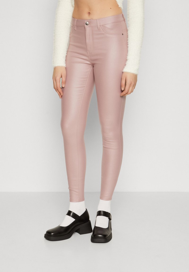 Pantalon en simili cuir rose à la texture lisse et à la coupe slim, associé à des chaussures Mary Jane noires et des chaussettes blanches.