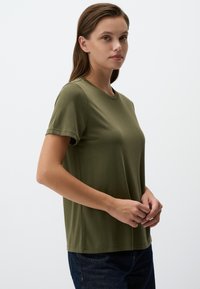 T-shirt verde oliva a maniche corte in morbido materiale con scollatura rotonda e vestibilità rilassata, caratterizzato da bordi puliti e cuciture minime.
