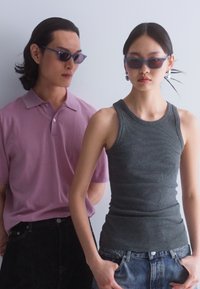 Camisa polo morada y camiseta sin mangas gris llevadas por dos personas. La camisa polo tiene un cuello abotonado; la camiseta sin mangas es ajustada. Ambos llevan gafas de sol.