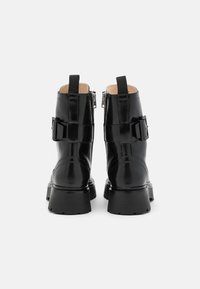 Botines de charol negro con suela gruesa, cremalleras laterales y detalles de hebillas ajustables para un ajuste seguro. Acabado texturizado.