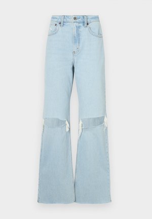 Šviesiai mėlynos džinsinės plačios kojos kelnės su kelių išpjovomis, suplėšytais kraštais ir aukštu liemeniu. Yra priekinis mygtuko ir užtrauktuko uždarymas, klasikinis penkių kišenių dizainas.