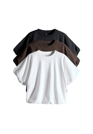 Giovane donna in piedi contro un muro bianco indossa un top nero a maniche corte, jeans blu scuro a gamba larga e ballerine nere con motivo.