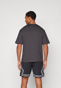 Mørkegrå bomulds T-shirt med rund hals og korte ærmer, kombineret med sorte shorts med hvid kant og sidelister.