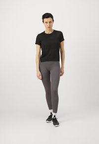 Svart kortermet treningstrøye kombinert med grå leggings. T-skjorten er lett, mens leggingsene sitter tett til kroppen med en jevn tekstur.