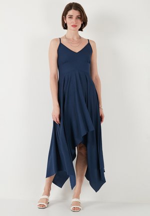 Navy blue, ankle-length dress made of textured fabric, featuring thin straps, a fitted bodice, and an asymmetrical hemline.
