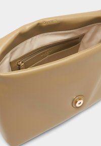 Interno di borsa in pelle beige con una texture liscia, dotata di una tasca con zip e chiusura con bottone color oro. Logo del marchio impresso.