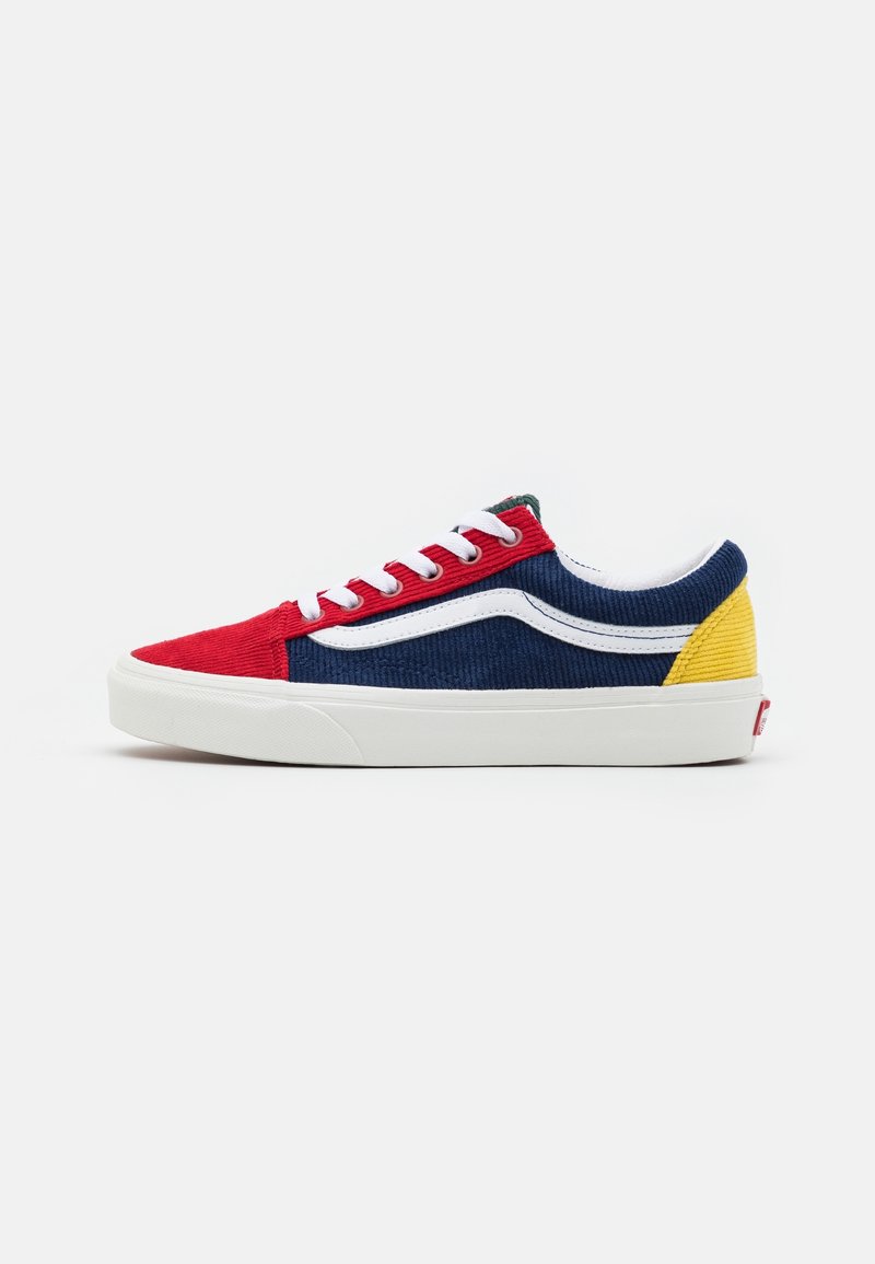 Zapatilla de pana roja y azul con cordones blancos, franja lateral blanca y detalle amarillo en el talón. Suela de goma blanca con agarre texturizado.