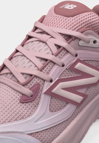 Κοντινό πλάνο ροζ αθλητικού παπουτσιού New Balance με ύφασμα από δίχτυ, υφασμένο πέλμα και κορδόνια δεμένα σε τυπικό διαγώνιο σχέδιο.