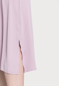 Vestido lilás claro com uma textura suave, apresentando fendas laterais e uma bainha limpa. O tecido cai suavemente com mínimo brilho.