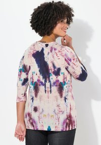 Bunte, weiche Stoffoberteil mit rundem Ausschnitt, Dreiviertelärmeln und einem abstrakten Batikmuster in lila, blau und pink.
