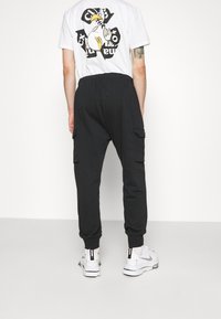 Svarta cargobyxor med elastisk midja, sidofickor och avsmalnande ben. Kombinerat med en vit T-shirt med grafisk design.