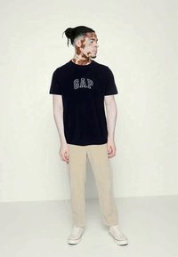 Camiseta de logo de GAP en azul marino, con mangas cortas y corte relajado. Combinada con pantalones rectos beige y zapatillas blancas. Diseño simple y casual.