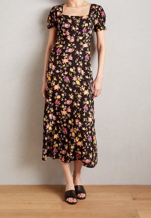 Robe maxi noire à fleurs avec des manches courtes bouffantes, ornée d'un imprimé rose et jaune. Assortie avec des sandales à talons ouverts noires.