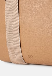 Skórzana torba w kolorze tan z textured wykończeniem, z wplecionym paskiem z kremowym akcentem i małym wytłoczonym logo w rogu.