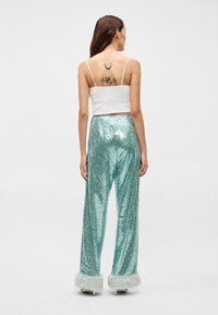 Σεquin παντελόνια σε τουρκουάζ χρώμα με φαρδιά πόδια και αφράτη, λευκή επένδυση. Φοριέται με εφαρμοστό λευκό τοπάκι. Ορατό τατουάζ στην πλάτη.