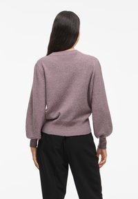 Lila pletena jopica z dolgimi, napihnjenimi rokavi in ribastim robom, z okroglo odprtino za vrat in mehkimi vlakni, v kombinaciji s črnimi hlačami.