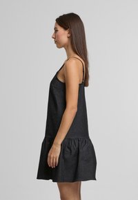 Melnas džinsu kleitas ar regulējamām siksnām, pieguļošu korseti un izplestu volāna apakšu. Gluda tekstūra, vidus augšstilba garumā.