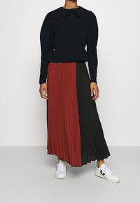 Blusa blu navy con colletto rotondo e dettaglio in cravattino abbinata a una gonna plissè a blocchi di colore rosso e nero. Le sneakers bianche completano il look.