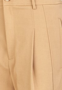Beige broeken gemaakt van textuurstof, met plooien, een knoopsluiting en zijzakken voor functionaliteit. Strak ontwerp met een neutrale kleur.