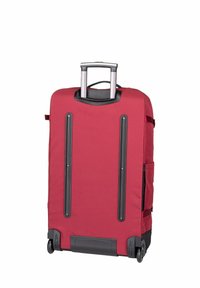 Valise à roulettes rouge avec un extérieur en tissu durable, une poignée rétractable, deux accents noirs verticaux, et deux poches latérales.